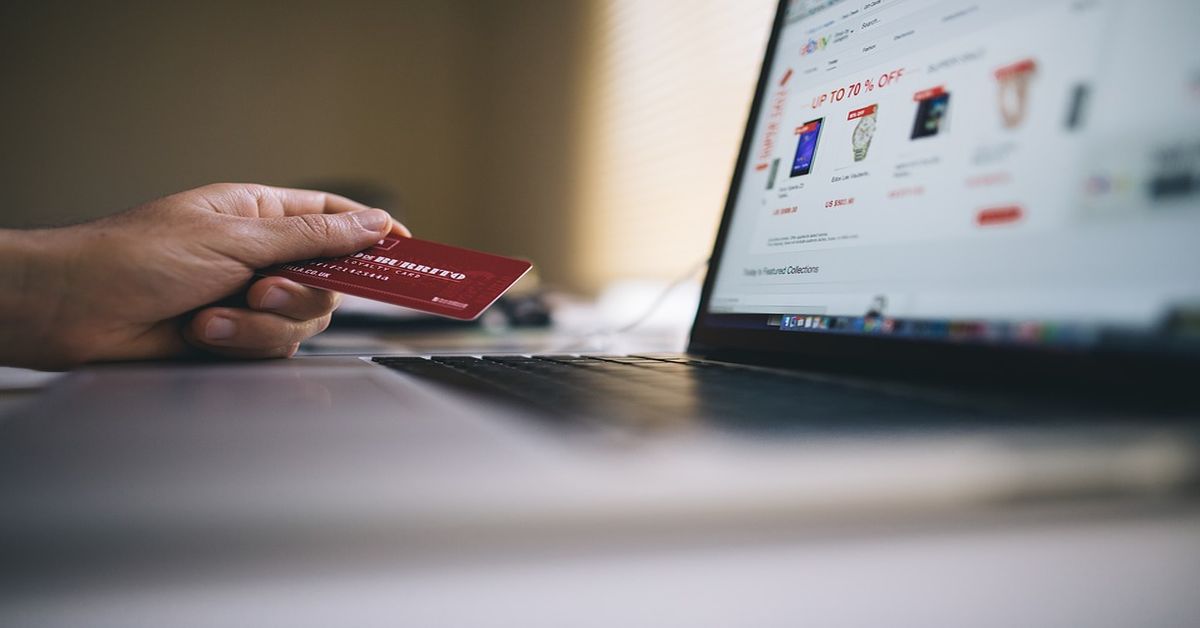 imagem de uma mão segurando um cartão de crédito em frente um computador com uma página da internet aberta em um site de compras