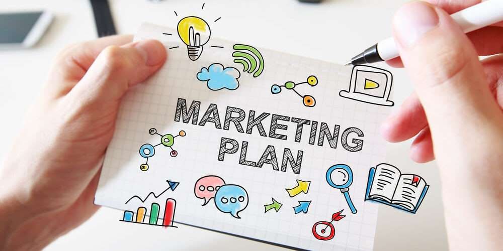 Uma pessoa segurando uma folha de papel com alguns desenhos e a palavra Marketing Plan ao centro