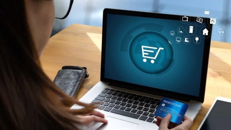 Imagem de uma mulher segurando um cartão de crédito e efetuando compras em um e-commerce