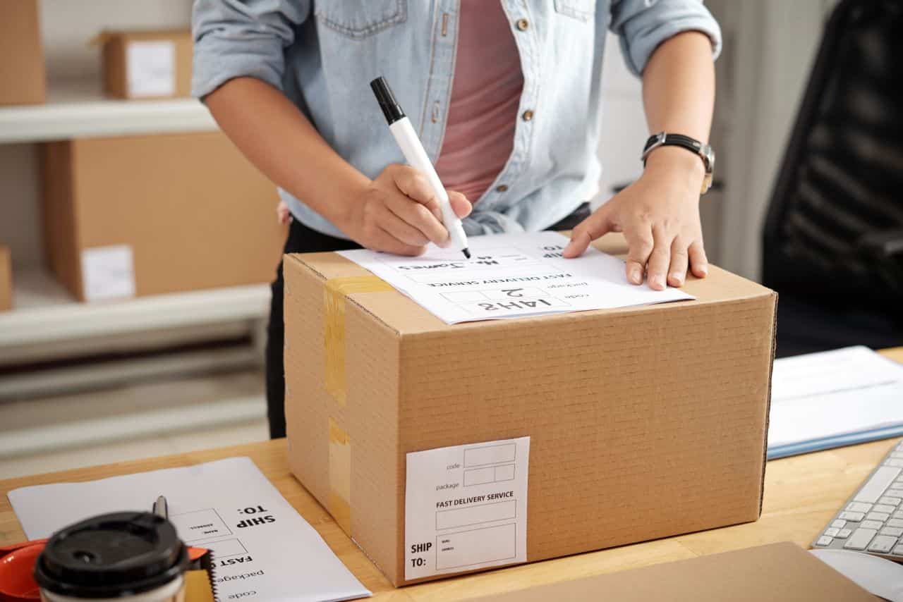 Imagem de uma pessoa fazendo uma anotação em caixa de papelão para a entrega do produto