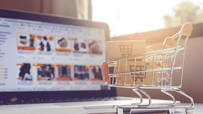 Imagem de uma miniatura de carrinho de supermercado sobre um notebook, com a página de um e-commerce aberta