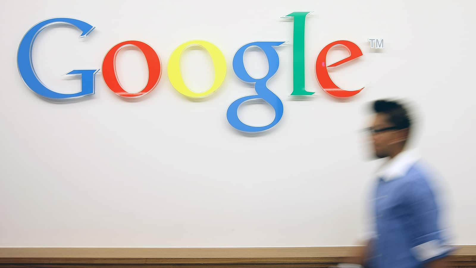 Imagem da palavra Google colorida pintada em uma parede com uma pessoa desfocada passando por ela