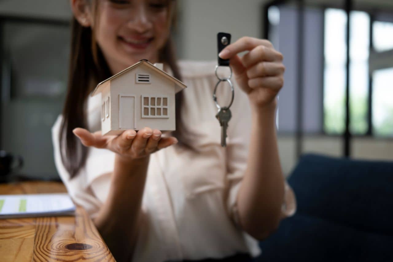 Imagem de uma mulher segurando uma miniatura de casa em uma mão e uma chave em outra
