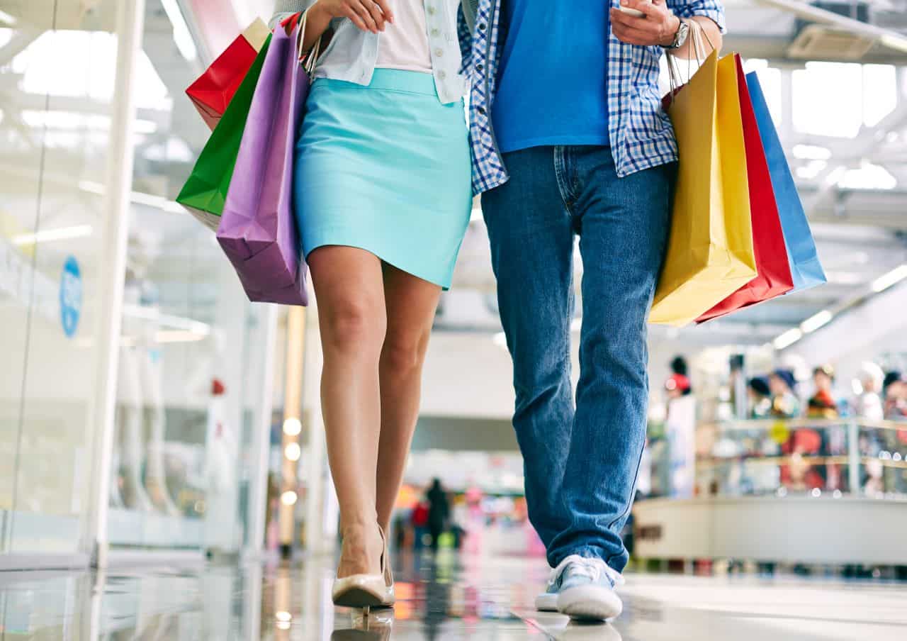 Imagem de um casal andando no shopping segurando sacolas de compras