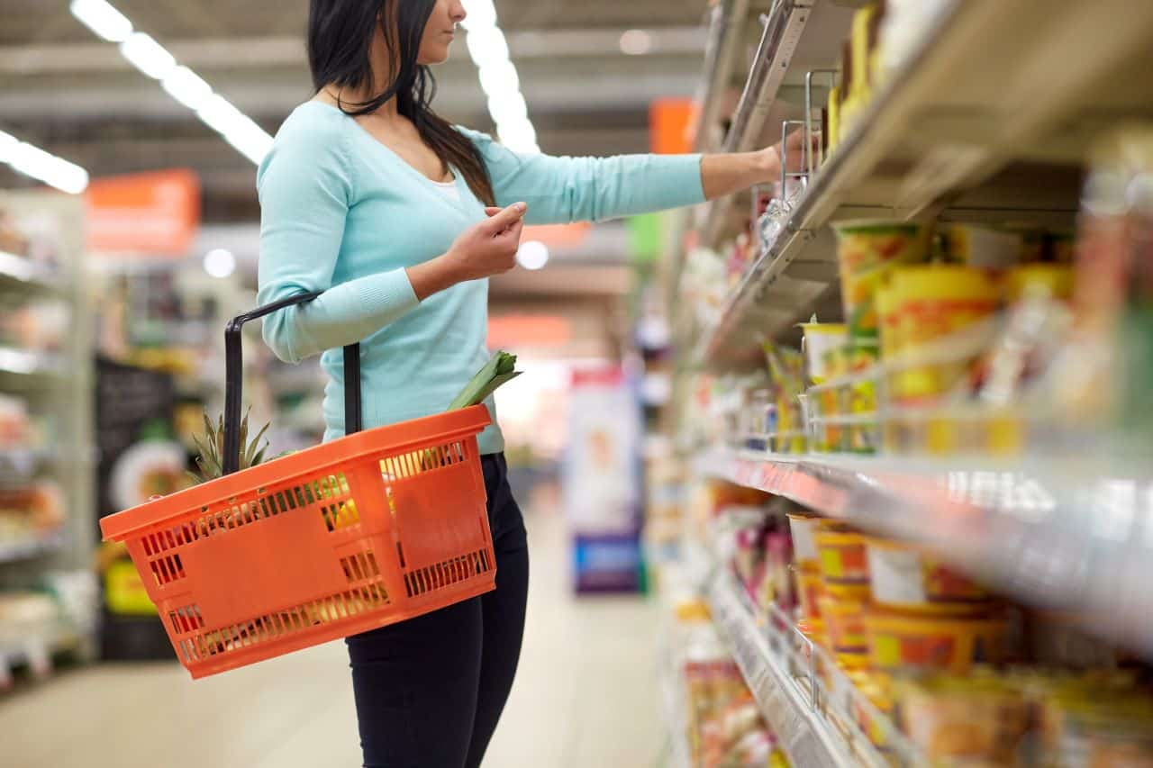 Imagem de uma mulher no supermercado segurando uma cesta com alimentos